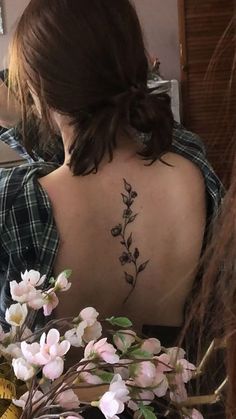 a woman with a tattoo on her back is sitting in front of a flower arrangement