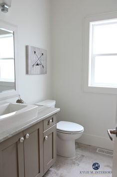 a white toilet sitting next to a bathroom sink under a window on top of a tiled floor