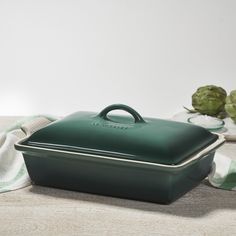 a green casserole dish sitting on top of a table next to cauliflower