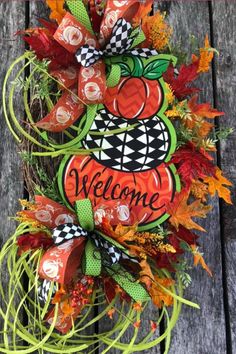 a welcome fall wreath with an orange pumpkin and checkered bow on it, sitting on a wooden surface