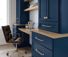 a chair sits in front of a desk with blue cabinetry and gold pulls on it