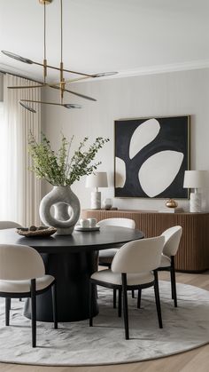 a dining room table with white chairs and a vase on top of it in front of a painting