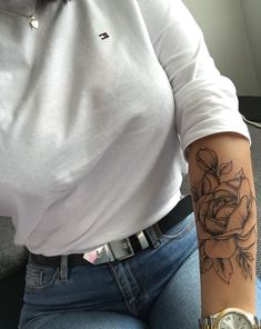 a woman with a rose tattoo on her arm sitting down and holding onto a watch