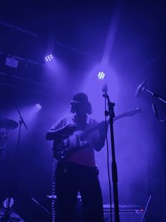 a man standing in front of a microphone on top of a stage holding a guitar