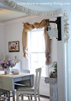 a table and chairs in a room next to a window with curtains on the windowsill