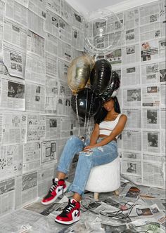 a woman sitting on top of a pile of newspapers with balloons attached to her head