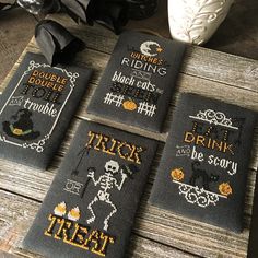 four cross - stitch halloween coasters on a wooden table next to a white vase