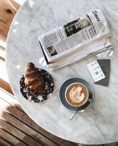 there is a cup of coffee and a croissant on the table next to it