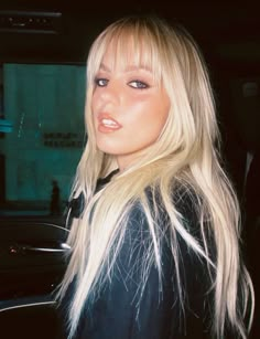 a woman with long blonde hair and blue eyes posing for a photo in a car