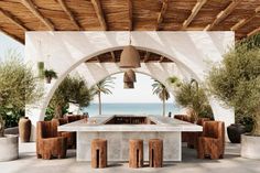 an outdoor dining area overlooking the ocean with wooden tables and stools on either side