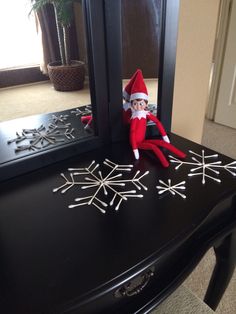 an elf sitting on top of a table next to a mirror and snowflakes