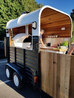 a food truck with a woman preparing food in it's back end and wood paneling on the side