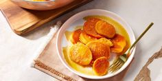 a white plate topped with sliced oranges next to a bowl filled with sauce and a fork