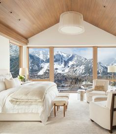 the bedroom is decorated in white and has mountain views from it's large windows