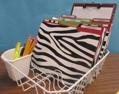 a basket filled with zebra print binders and pencils on top of a wooden table