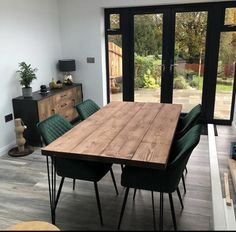 a dining room table with green chairs in front of large glass doors that look out onto the back yard