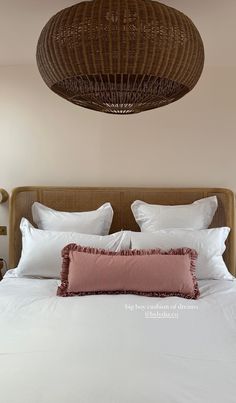 a bed with white linens and pillows under a wicker light fixture above it