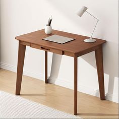 a wooden desk with a laptop on it and a lamp next to the table in front of it