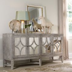 an ornately decorated sideboard with glass doors in a white living room, next to a window