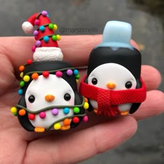 two small penguins wearing christmas hats and scarfs are held in someone's hand