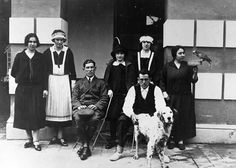 an old black and white photo of people posing with a dog in front of a building