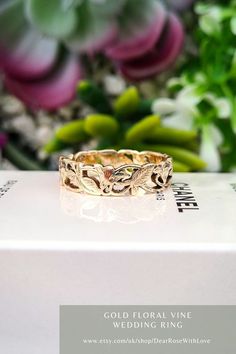 a gold wedding ring sitting on top of a box with flowers in the back ground