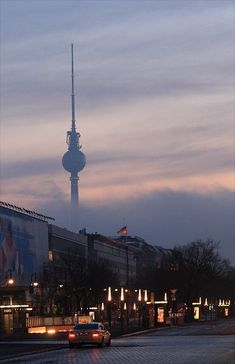 a car driving down a street in front of a tall building with a tv tower