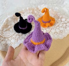 three crocheted witches sitting on top of a white doily next to a person's hand