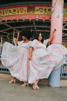 two women in long dresses standing next to each other near a carnival ride at the same time