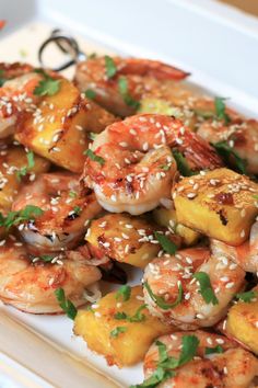 shrimp and pineapple skewers with sesame seeds on a white platter, ready to be eaten