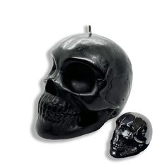 a black candle with a skull on it next to a smaller one in the shape of a skull