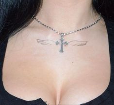 a close up of a woman's chest with a cross and wings tattoo on it