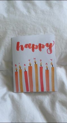 a birthday card with candles on it sitting on top of a white sheet covered bed