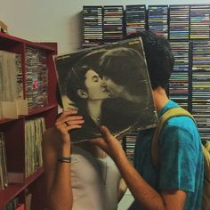 a man holding up a record in front of a woman's face with an album on it