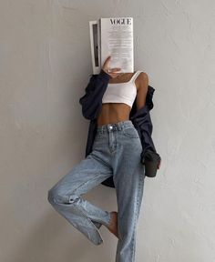 a woman leaning up against a wall while reading a magazine with her hands on her head