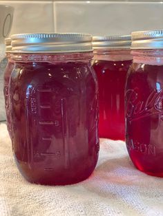 three jars filled with purple liquid sitting on top of a white cloth covered tablecloth