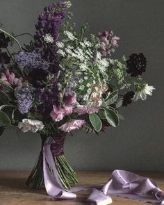 a vase filled with purple and white flowers on top of a wooden table next to a pair of shoes