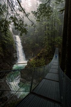 a suspension bridge over a river with a waterfall in the background