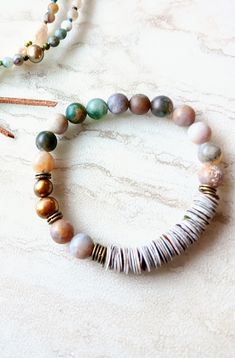 First, at almost 22" in length, this beaded strand can be worn as a necklace and a triple wrap bracelet if you like. Muted greens, grays, beige, gold, desert rose, touches of orange, rust, army green, beige, and more. A great mix of washed out color like a beaten ocean landscape. 6mm to 11mm Pearl, matte 4mm Moss Agate, matte Sunstone, matte 4mm  Jasper stones, and accents of seed beads, and metals. Distressed natural suede loops and coconut button closure make extendable. One-of-a-kind. The ite Bracelet Pearls, Single Bracelet, Triple Wrap Bracelet, Ocean Landscape, Hippie Necklace, Up North, Bone Beads, Oyster Shell, Lovely Necklace