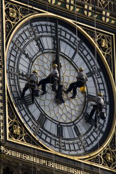 three men working on the face of a large clock tower with gold trimmings