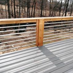 a wooden deck with metal railing and trees in the background