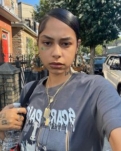 a woman with tattoos on her face standing in front of a fence holding a cup