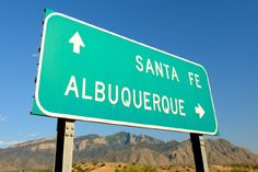 a green street sign pointing to santa fe and albuqueroque with mountains in the background