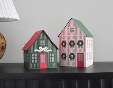 three paper houses sitting on top of a black table next to a lamp and wicker basket