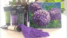 purple gloves and paint are sitting on a table next to a potted plant in front of a painting