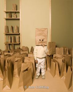 a small child is standing in a room with paper bags on the floor and wearing a bag over his head