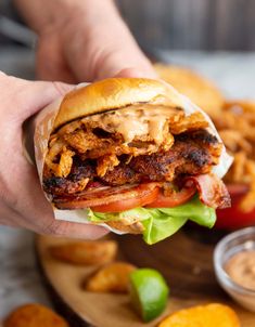 a person is holding up a sandwich with meat and lettuce in front of some french fries