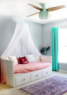 a bedroom with a canopy bed, pink and white bedspread, blue drapes and rug