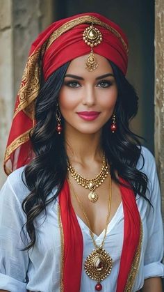 a woman wearing a red and gold head piece with jewelry on her neck, standing in front of a stone wall