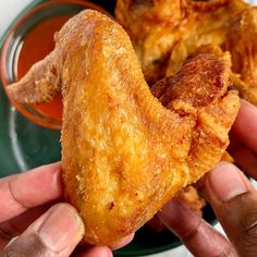 two hands holding fried food in front of a bowl with sauce on the other side